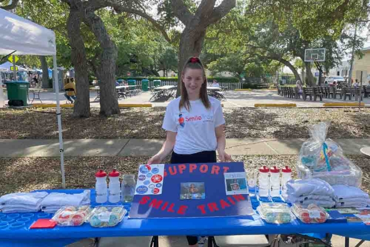 Alexandra smiling and standing with a Smile Train support sign at a table