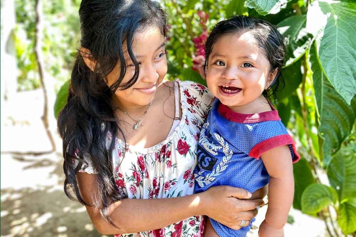 A smiling Lupe holds her joyful little brother José