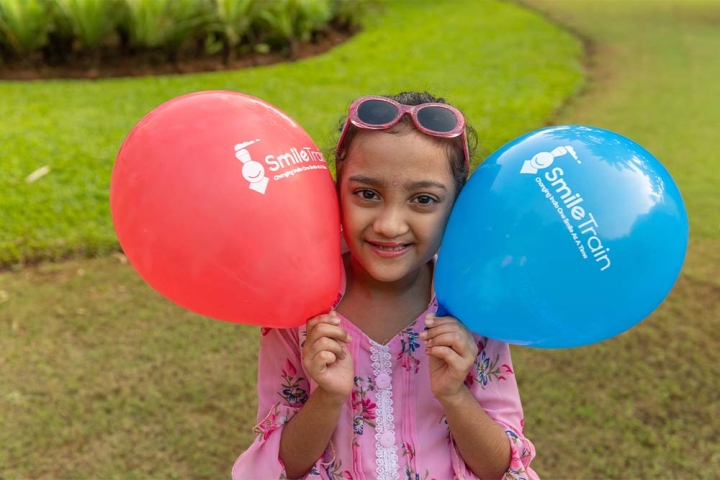 Durva smiles and holds up two Smile Train balloons