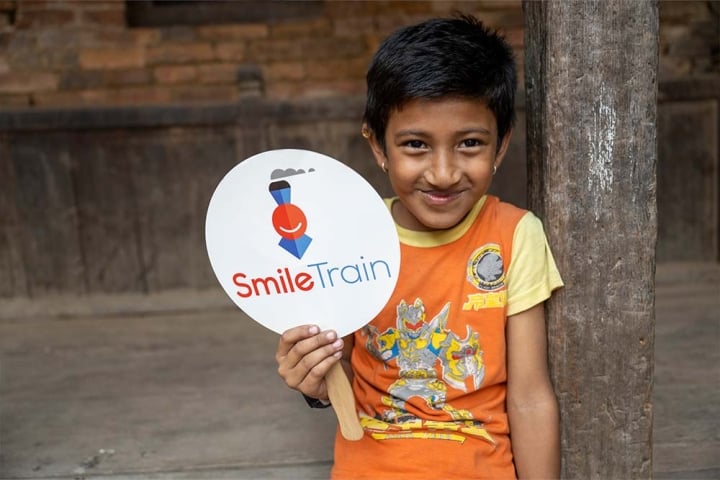 Aarosh grins and holds up a Smile Train paddle logo