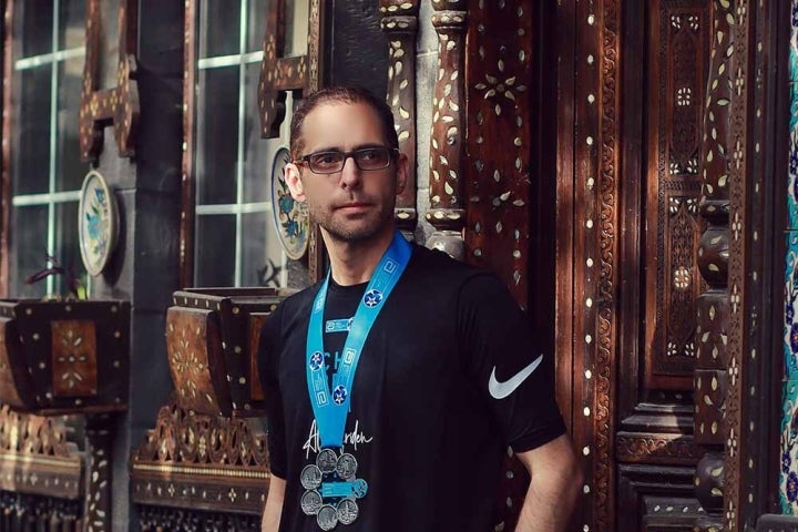 Aladdin Meriden standing against a colorful wall in the Old City of Damascus wearing his six World Marathon Majors medals