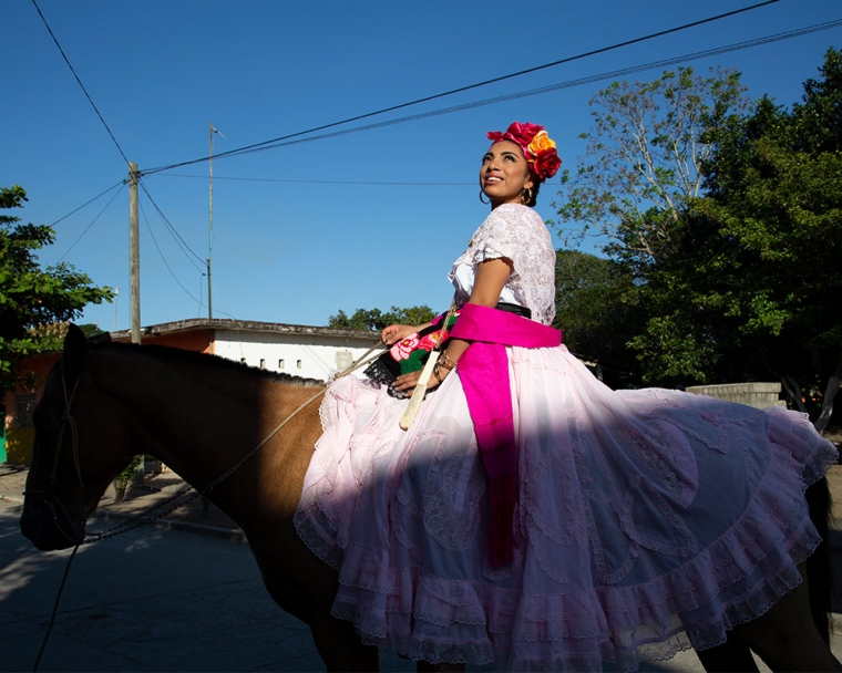 Adahara riding a horse through her town dressed in traditional Mexican garb.