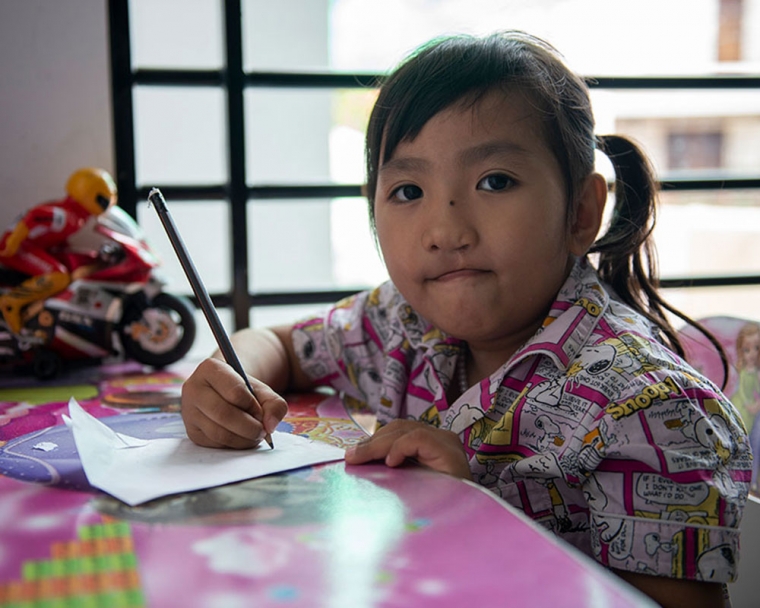 Meng writing at a desk after her cleft lip and palate treatment.