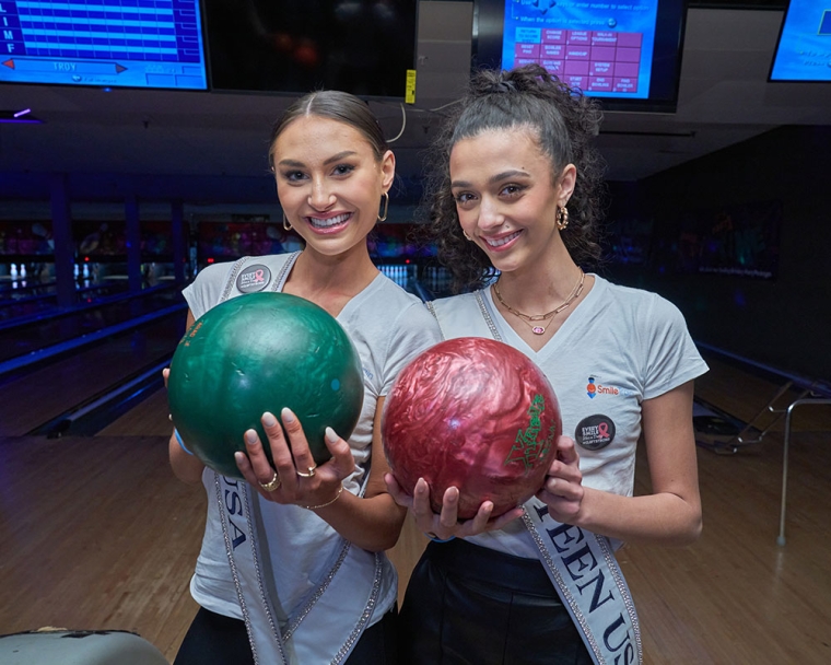 Miss Teen USA and Miss USA smiling and holding bowling balls