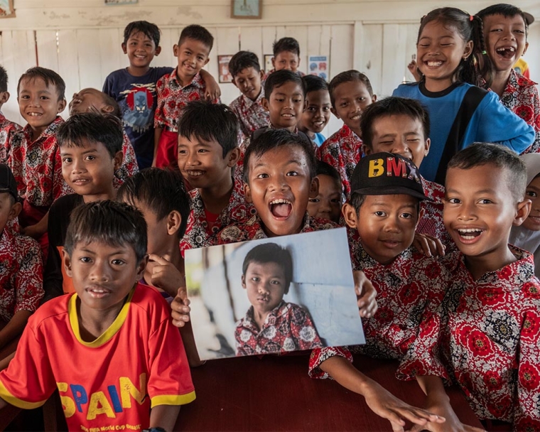 Rajib smiling with his friends and holding a photo of himself before cleft surgery