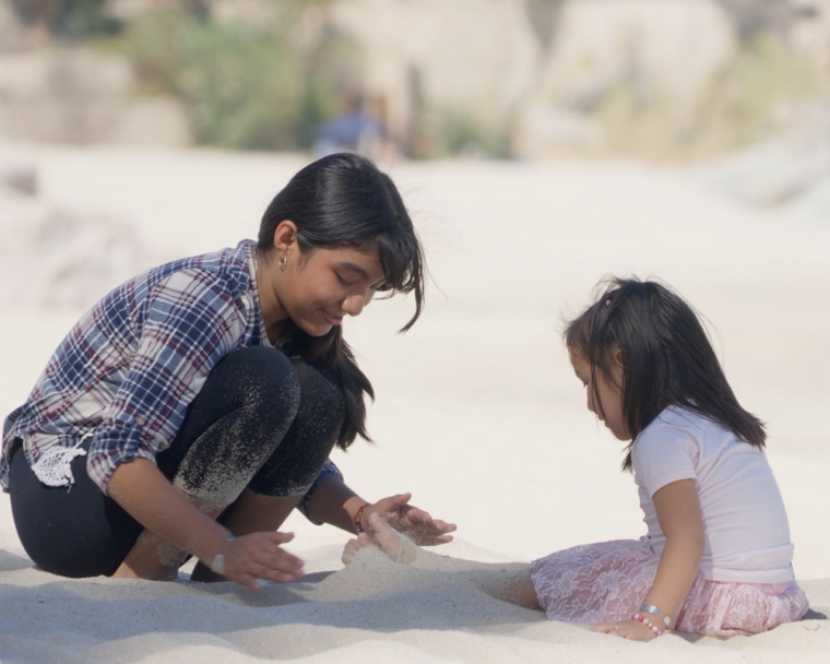 Adriana plays in the sand at the beach with her little sister
