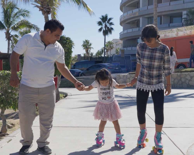 Adriana and her father hold her little sister’s hands as the two girls roller skate down the street