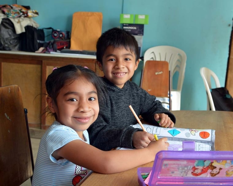 Astrid and her brother take a break from working on their coloring book to smile at the camera.