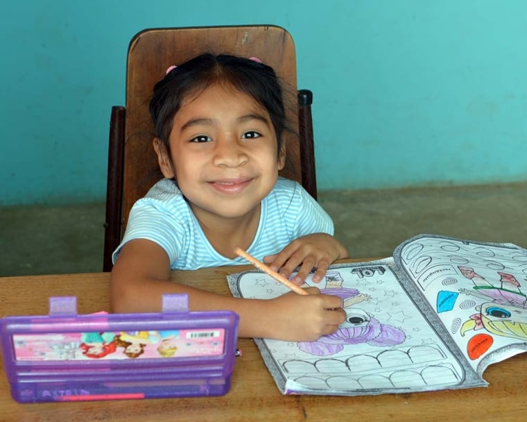 Astrid grins up at the camera, working on her coloring book.