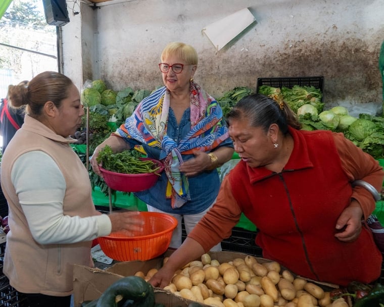 Lidia holding a basket of greens while shopping with other women