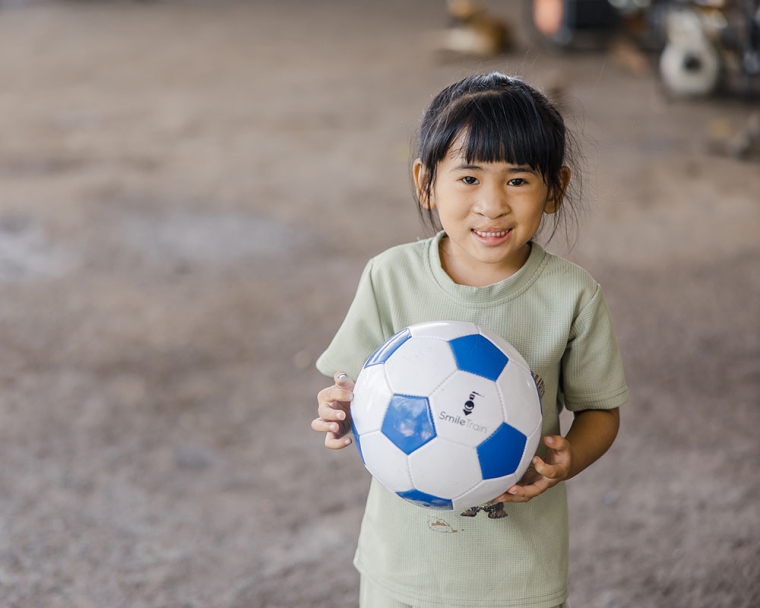 Niu smiling and holding a soccer ball after cleft surgery