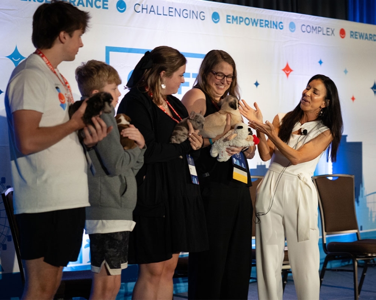 Four Cleft Con participants stand on stage, each holding a puppy with a cleft